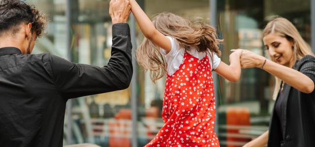 Parents holding their child's hands. The child is jumping